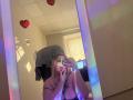 DiLaria with blonde hair, wearing a towel on her head, taking a mirror selfie with rainbow lights, showing her tits and a tattoo on her chest.