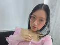 SophieDelaney with black hair, pink glasses, nose ring, and pink sheer top, showing her tits, with a hand on her chest. She's looking at the camera, smiling.