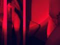 Red-lit mirror selfie of Tisia with her tits and pussy visible, wearing lace lingerie, her hand covering her mouth, reflection showing her ass and thigh.