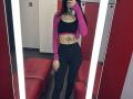 Tsukerberg, with dark hair, takes a mirror selfie in a brightly lit changing room. Wearing a pink jacket, black crop top, and black pants, exposing a colorful belly tattoo. Fucking hot.
