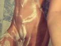 SarahFontain's wet, soapy tits and ass covered in white bubbles, with soap suds running down her tan, muscular, and glistening skin in a tiled shower.