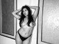 Celeste Morel se tient nue sur le torse, les mains dans ses cheveux foncés, portant des sous-vêtements noirs, mettant en valeur ses seins et ses fesses, regardant sur le côté, sur une photo en noir et blanc..