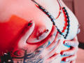 JadeMilleer's tits with red paint, nipple piercings, and tattooed hand holding them. Beaded necklace, painted nails, and red lighting. Her hands are gripping her tits firmly.