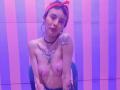 LaurenEvie69 with topless, shiny skin, small tits, tattoos on chest and arm, red bandana, choker, sitting on chair, pink and purple striped background, slightly leaning forward.