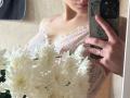 DominicaChambley's tits in a pink lace bra, holding white chrysanthemums, taking a mirror selfie with her phone, showing a ring on her finger.