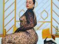 LunaSoler in black lace bodysuit, showing her tits and ass, sitting on bed, glasses on, red lipstick, dark hair up, gold earrings, yellow pillows, black high heels.