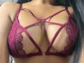 LilyConorr's tits in a deep red lace bra with strappy details and metal rings, showing a lot of cleavage and her smooth brown skin.