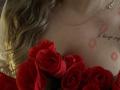 Niferttiti's tits with red rose tattoos and lipstick marks, gold necklace, and blonde hair. Red roses in foreground.