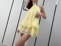 JuliannaMoor wearing a sheer yellow dress, standing with one hand on her belly, showing her ass, in a minimalist room with white walls and black lines.