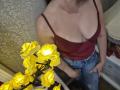 Rouzi with big boobs in a red tank top and blue jeans, holding a yellow flower lamp, her hand on her crotch. Her skin is light, her head is out of frame.
