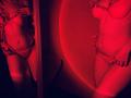 Tisia's red-lit reflection shows her in lace panties and a bra, with her hand on her thigh. Her tits are medium, her ass is curvy, and she's wearing thigh-highs.
