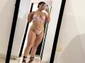 LorensDouce stands in a mirror selfie wearing pink lace lingerie with a bra and thong, showing her full-ass and thick thighs, holding a phone, in black strappy heels.