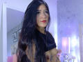 LuciadelaVega with long black hair, red lipstick, tattoos, and a black top pulled up, exposing small bare tits. She's wearing a nose ring and a gold necklace.