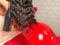 Niferttiti's shiny red latex butt is prominently in frame. She has long, wavy black hair with a red and black hairpiece. Her back is to the camera.