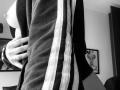 black-and-white photo of SujannaVarma's side, showing her hand on her dark track jacket with white stripes, exposing her bare tits, slightly visible in the frame.