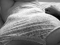 ScarletOra's curvy ass in floral lace panties, lying on bed, wearing a tight tank top, right hand resting near head, black and white photo, focus on lower body.