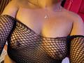 LilithAndAsmodeo's tan skin, medium-sized tits, visible nipples, wearing a black fishnet top, necklace with an "M" pendant, her head out of frame.