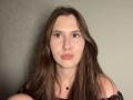 DeborahHaughey has long brown hair, pale skin, and pouty lips. She's wearing an off-shoulder black top with a small cross necklace. Her eyes are slightly upturned.