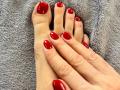 MikyWayxy's shiny red-painted toes and nails, with matching red-painted fingers, resting on a gray textured surface. Hands and feet are positioned side by side.