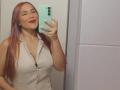 AntoniaBrunni with red hair, wearing a white button-up shirt, showing her tits in a mirror selfie, holding a green phone, smiling with red lipstick.