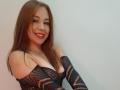JanneFlower with red hair, smiling, wearing a black, mesh, off-shoulder top, exposing her boobs. She has a nose ring and a necklace with a small pendant.