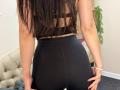 Stefanni's long black hair, wearing a black sports bra and high-waisted black leggings, shows her ass while standing with hands on her hips in a room.