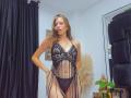 AnnaFer wearing a black, sheer lace lingerie dress with vertical beads, showing her small tits and black thong with a red bow, standing in a room with black curtains.