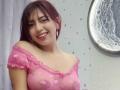BrendaaPierce with red hair, smiling, wearing a sheer pink top with heart patterns, showing her small tits through the fabric. She's standing near a moon-shaped wall decoration.