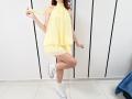 JuliannaMoor with pale skin, red hair, wearing a yellow halter dress, white socks, and white sneakers, standing on one leg, holding dress fabric.