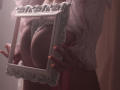 RosaVance holds a white, ornate frame in front of her big, bare tits. She's wearing a pink lace bra and has orange-painted nails. Soft, pinkish lighting.