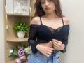 Rioria with long brown hair, black sheer top, exposing her small tits, buttoning her jeans, standing in front, wearing hoop earrings, pouty face, wooden shelf with plant and dress.
