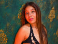 JaneKetty has long brown hair, pink lipstick, and a cute face. She's wearing a black, polka-dotted top with cut-out sections. Her ass is slightly visible.