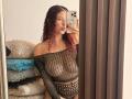 ValeryScot with red curly hair, wearing a see-through black mesh top, showing her tits and pussy, taking a mirror selfie with a phone in a bedroom.