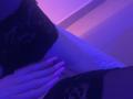 La mano di MissJulieDeux è appoggiata sulla sua vulva, coperta di pizzo nero, con un'illuminazione viola. Il suo sedere, anch'esso coperto di pizzo, è parzialmente visibile. Le sue dita toccano delicatamente la sua pelle..