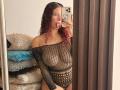 ValeryScot with curly red hair, tongue out, wearing a black fishnet one-piece, showing her tits and pussy through the mesh. Holding a phone in a mirror selfie.