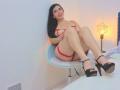 MaraLoop sits on a chair, legs up, wearing red lingerie with straps, black high heels, and smiling. She has long black hair, red lipstick, and her tits are visible.