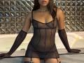 EmmaLatin in sheer black lingerie, showing small tits and a pierced pussy, with long brown hair, black gloves, and a pearl necklace, standing in front of a white tub.