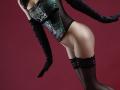 KamiLove wearing a green floral corset, black sheer gloves, and lace thigh-highs, with her ass and pussy partially visible, against a dark red background.
