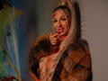 CelineDian with long blonde ponytail, wearing a fur coat, licking red lipstick off her finger, showing her tits, with red nail polish, and a sexy smile.