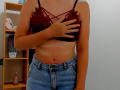 Steisii wears a sheer black lace bralette covering her small tits, with her right hand covering her chest. She's in high-waisted blue jeans, showing a tan line.