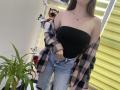 Nesie with bare shoulders, black tube top, and pink plaid shirt off, wearing blue jeans, standing by a plant, stuffed tiger, and butterfly decorations, visible tits, no face.