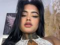 LairaHearvy with black hair, thick eyebrows, and eyeliner, wearing a lace top, showing a tattooed neck, and slightly parted pink lips. Her ass is not visible.