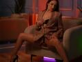 BabeInBlush with brown hair, tan skin, and black bra, sitting on a chair, legs spread, exposing her pussy, wearing an open tan blazer, black high heels, seductive expression.