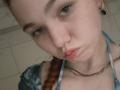 KatiRokisky has a pouty face with slightly parted pink lips, fair skin, blue eyes, and a braided red ponytail. She wears a blue tie-dye top and a silver chain.