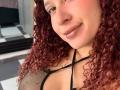 ValeryScot with curly red hair, brown eyes, and glossy pink lips, wearing a black mesh top, showing her tits, smiling softly, wearing a thin necklace.