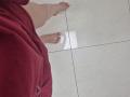 JoannaSia's bare feet with red-painted toenails standing on white marble tiles, wearing a red shirt. Her lower legs and feet are visible, with a slight shadow under.