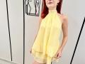 JuliannaMoor with red hair, wearing a yellow halter dress, showing her bare shoulders and a hint of her pussy under the sheer fabric. Her hands rest on her thighs.
