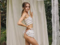 EvaDaly in a ruffled white tube top and matching skirt, standing sideways with hands on fabric, showing her ass and a subtle smile, with a cute, slim build.