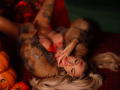 CelineDian lying on red carpet, wearing fur coat, blonde hair, red lipstick, and red nails, with hands near her tits, surrounded by pumpkins, eyes closed, looking sexy.