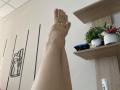 Olieri's bare feet with pink toenails are crossed in the air, showing off her smooth, pale skin. Shelves with plants and a white pot are in the background.